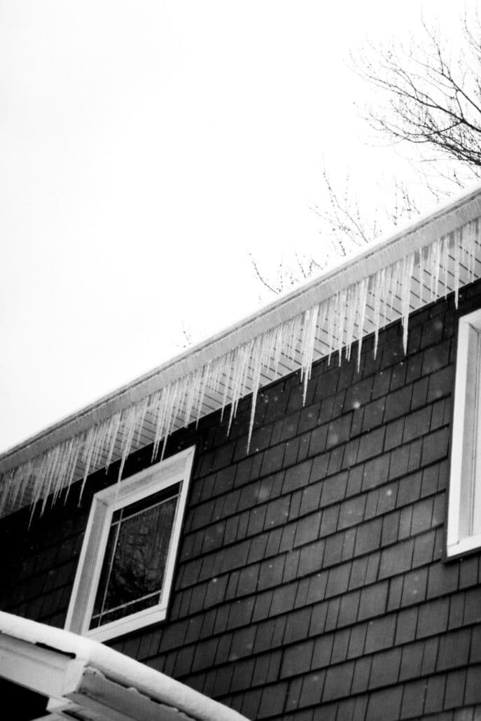 Icicles hanging from the edge of a snow-covered shingled roof, a sign of ice dam risk